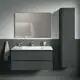 Wandmontierter Lotionspender in Chromoptik neben einem Waschbecken in modernem Badezimmer von Ideal Standard. Handtuch hängt an der Wand, Spiegel über dem Waschbecken.